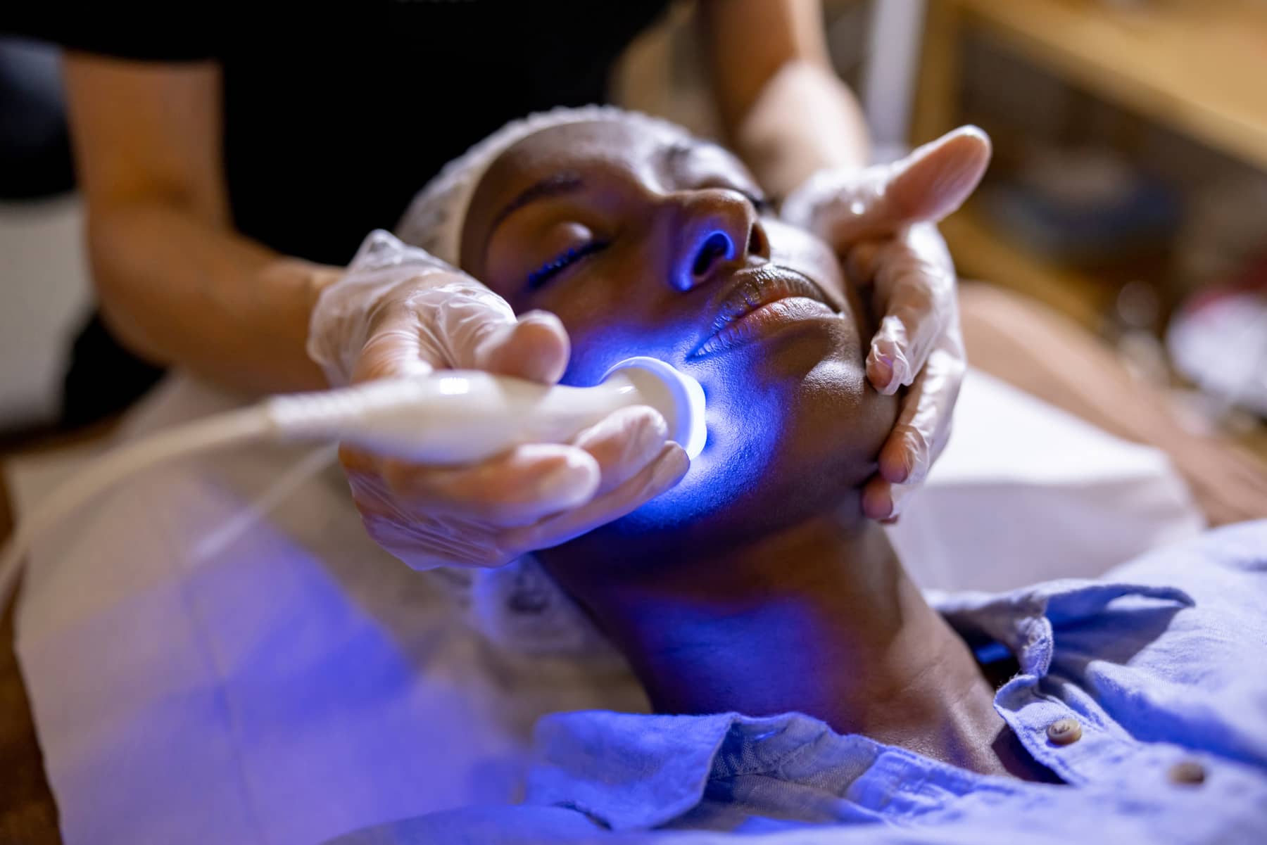 Esthetician performing a hydrating facial treatment on a relaxed client with LED light therapy.